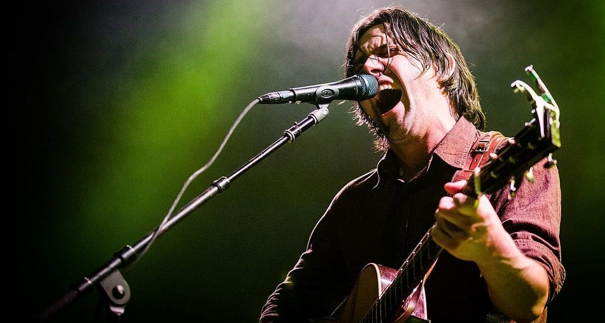 Conor Oberst playing guitar live, singing with his eyes closed